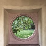 Blick durch ein Rundes Fenster i Wandelgang in den Moscheegarten, es sind Wiese und der Ast eines Baumes zu sehen.