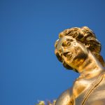 Goldene Skulptur der Böotische Atalante. zu Sehen ist nur der Kopf der sich vom strahlend blauen Himmel abhebt.